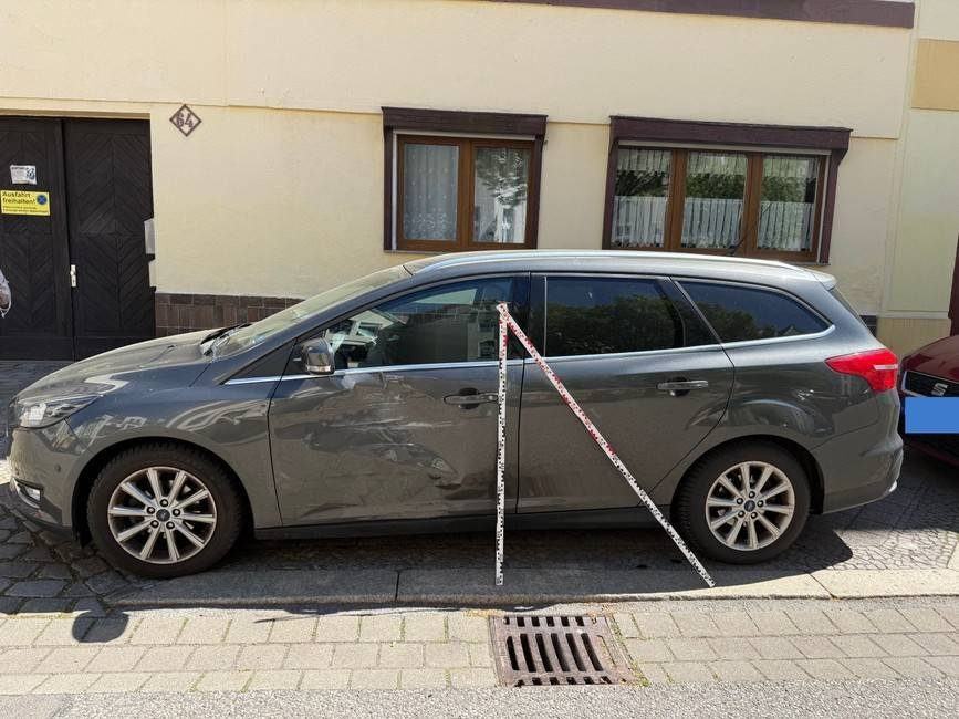 Übersichtsaufnahme der linken Fahrzeugseite: Schadensschwerpunkt an der vorderen Tür, Messlatte angelegt, Ford Focus Turnier Titanium (Leipzig), Schadenshöhe 4.294,51 € inkl. MwSt.