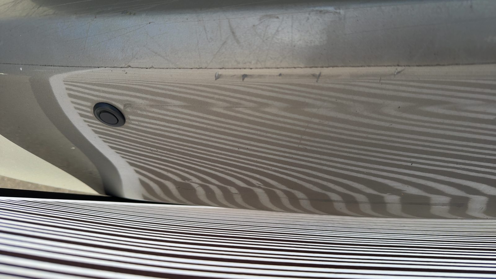 Verformter hinterer Stoßfänger neben dem Parksensor, mit Streifentafel sichtbar gemacht, Foto aus der Besichtigung